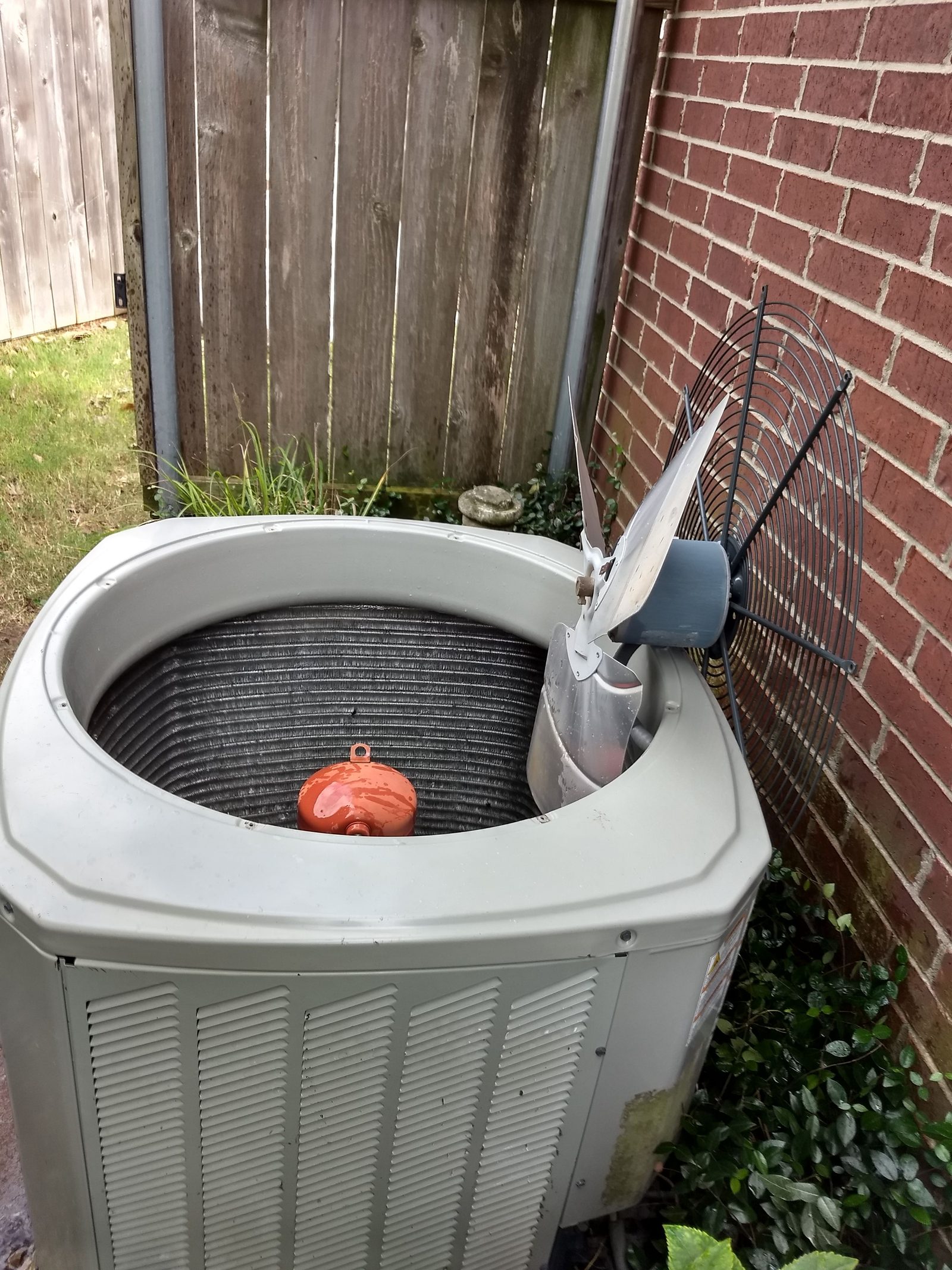 Condenser unit opened for service beside a brick wall with tools staged
